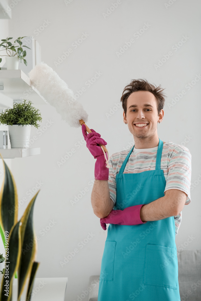 Young man wiping dust from shelf at home