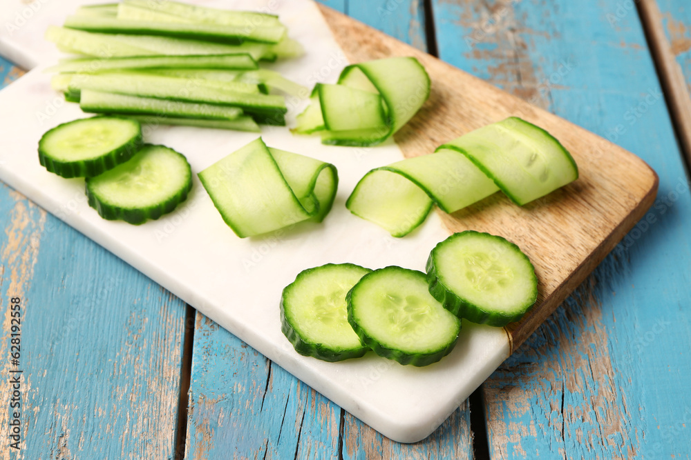 Board with fresh cut cucumber on blue wooden background, closeup