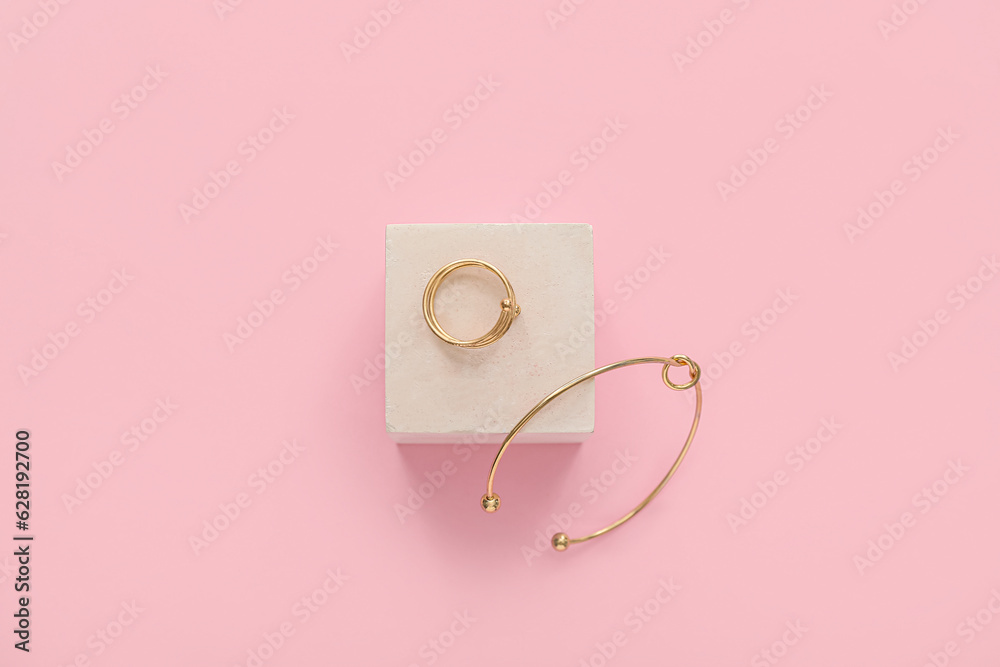 Showcase pedestal with golden ring and bracelet on pink background