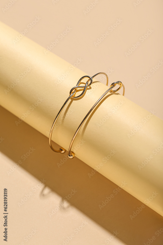 Rolled paper with golden bracelets on beige background, closeup