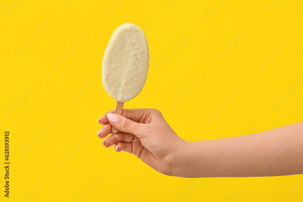 Woman holding delicious chocolate covered ice cream on stick against yellow background