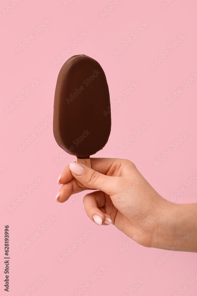 Woman holding delicious chocolate covered ice cream on stick against pink background