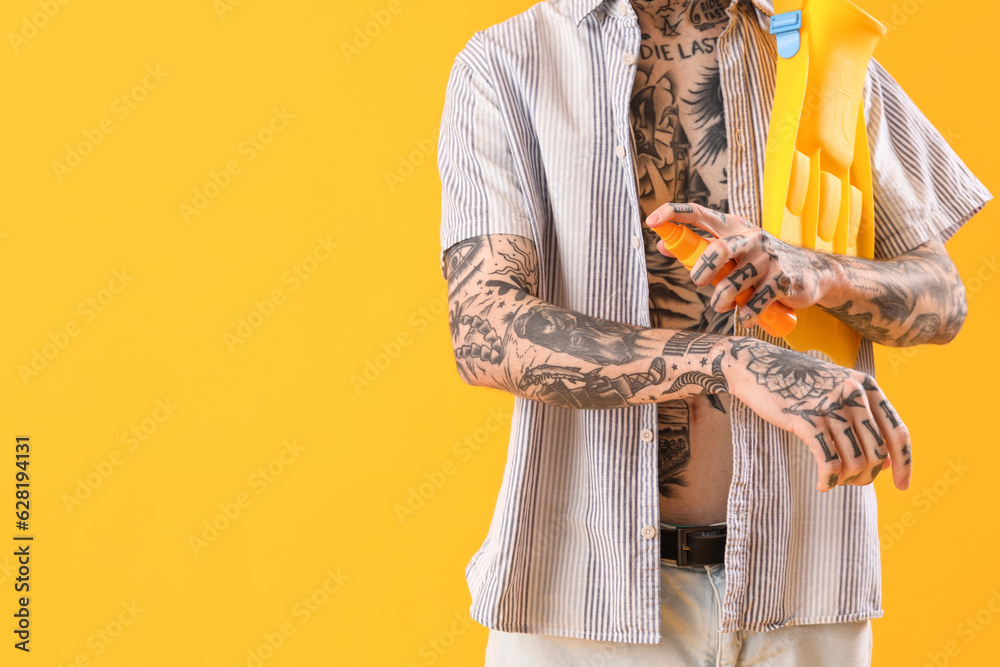 Tattooed man applying sunscreen cream on yellow background