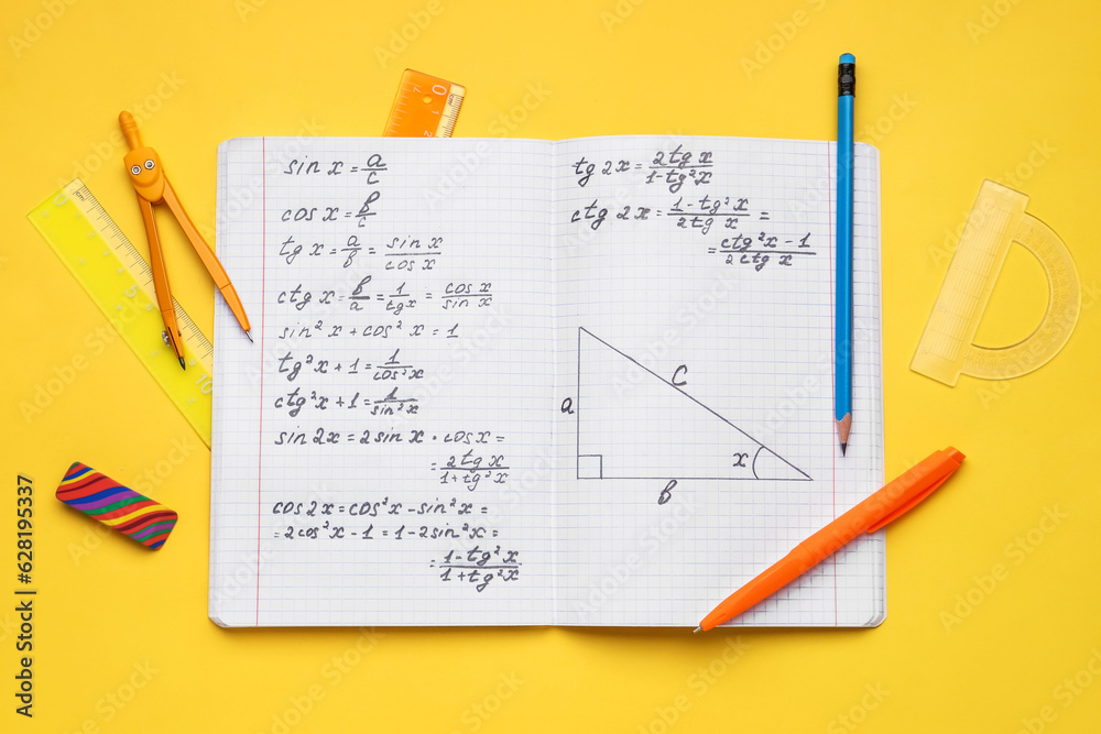 Copybook with maths formulas and stationery on yellow background