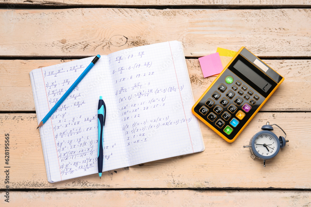 Copybook with maths formulas, calculator, alarm clock and stationery on beige wooden background