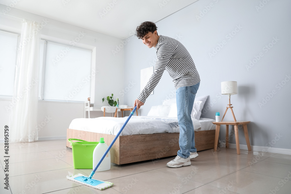 Young man mopping floor in bedroom