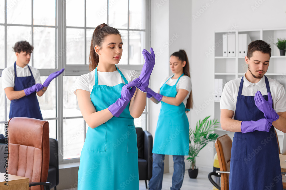 Young janitors putting rubber gloves in office