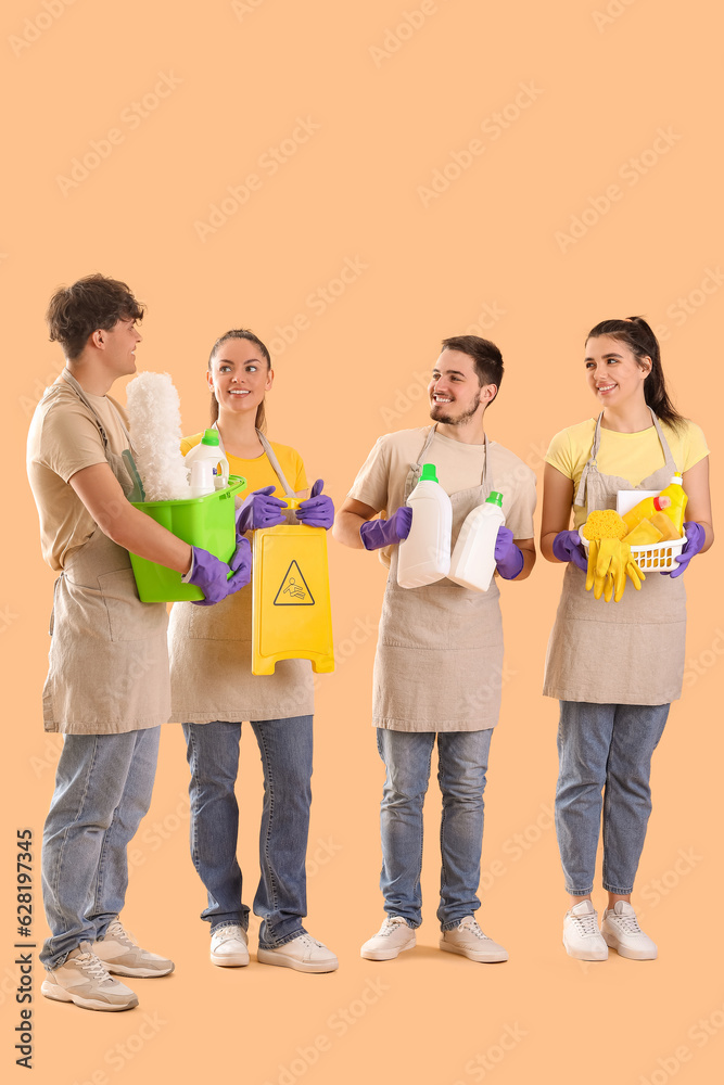 Young janitors with cleaning supplies on beige background