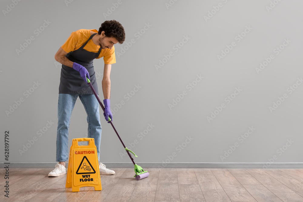 Young man mopping floor near grey wall