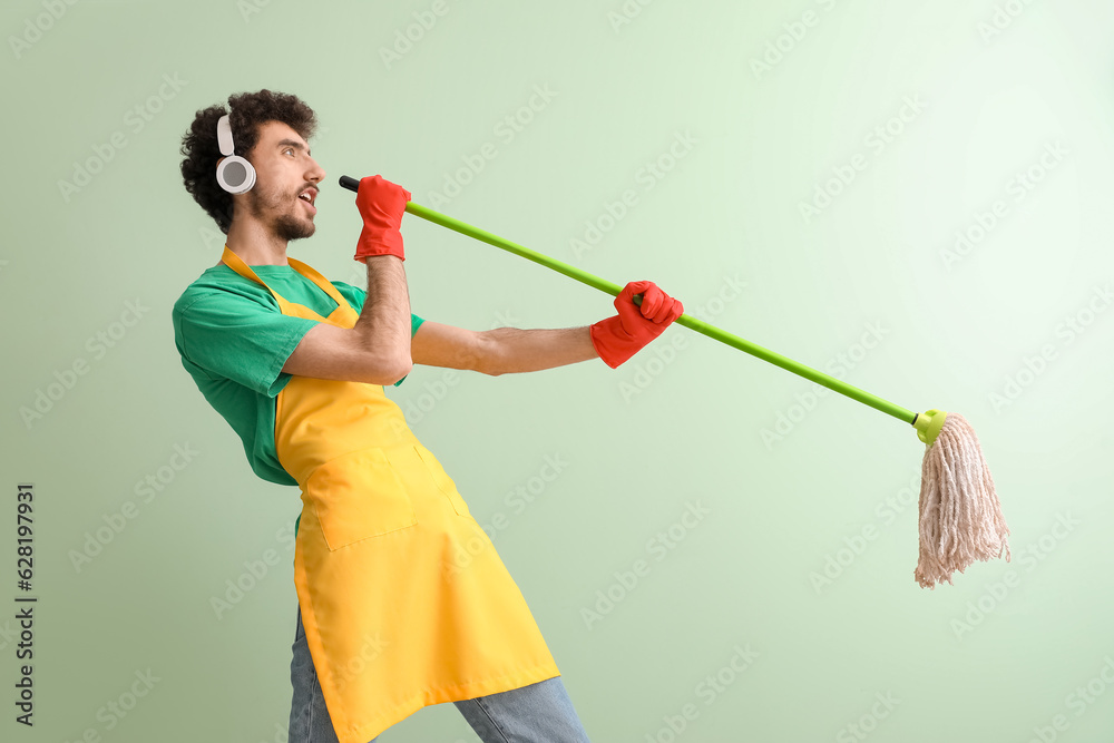 Young man in headphones with mop singing on green background