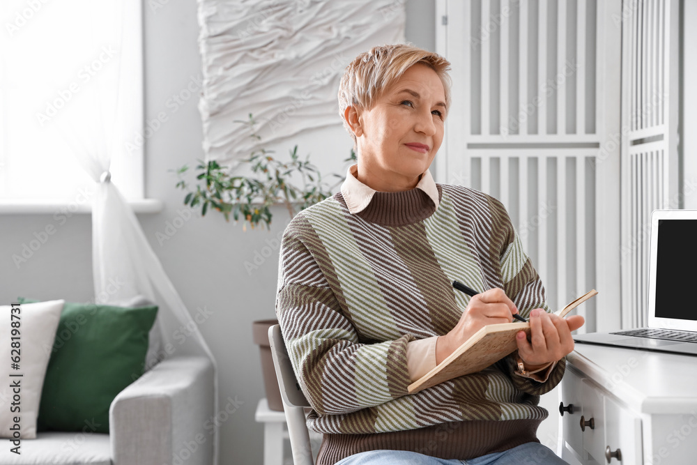 Thoughtful mature woman writing in notebook at home