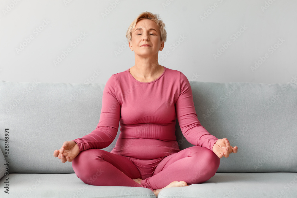 Mature woman meditating while sitting on sofa