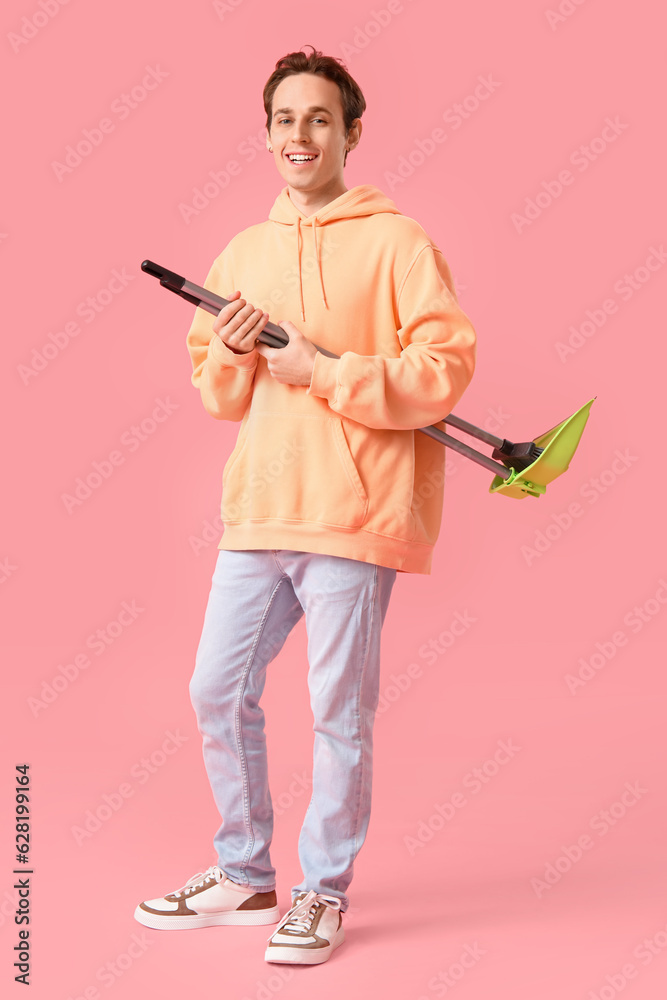 Young man with broom and dustpan on pink background