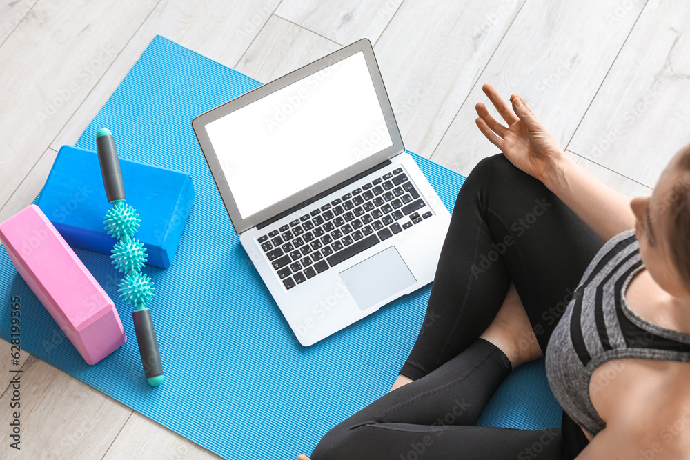 Sporty young woman with laptop doing yoga in gym