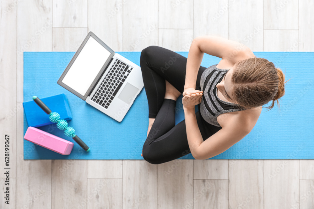 Sporty young woman with laptop doing yoga in gym, top view