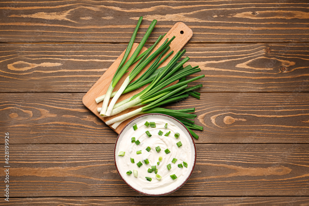 Bowl of tasty sour cream with green onion on wooden background