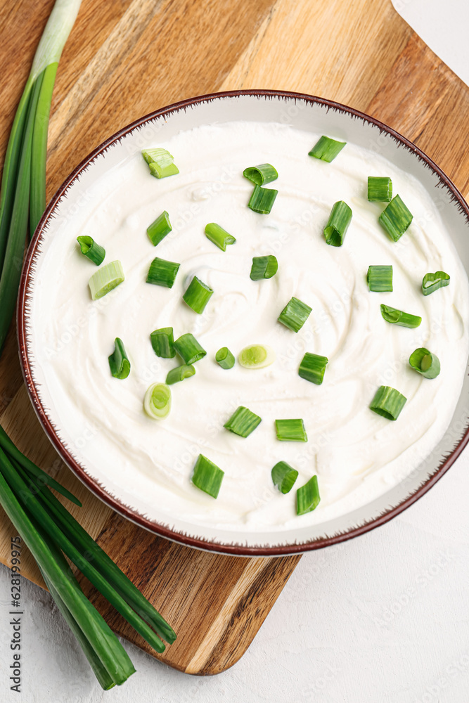 Bowl of tasty sour cream with green onion on light background