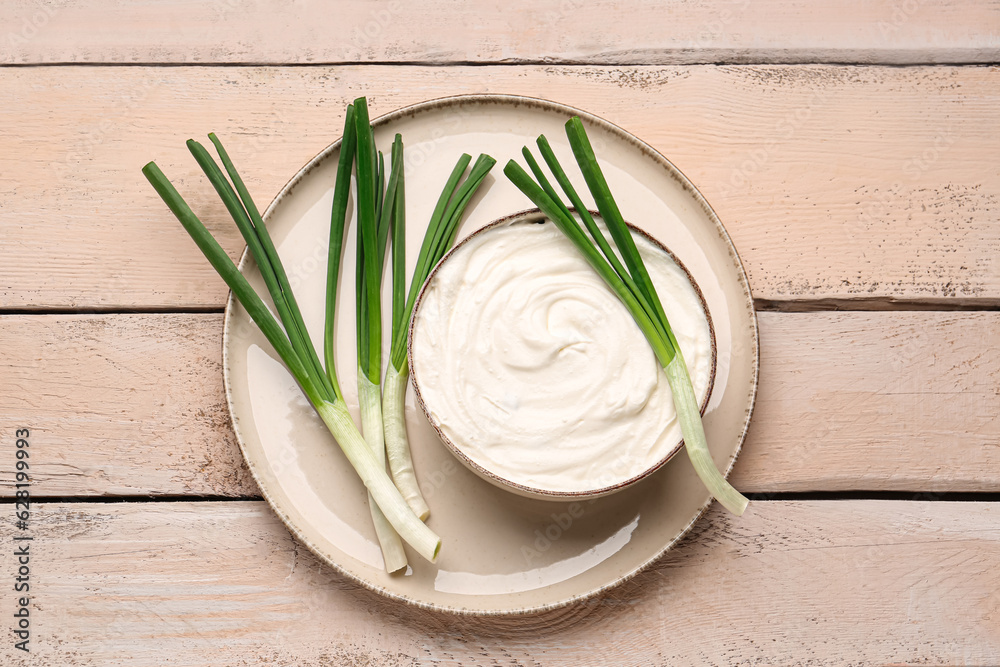 Bowl of tasty sour cream with green onion on light wooden background