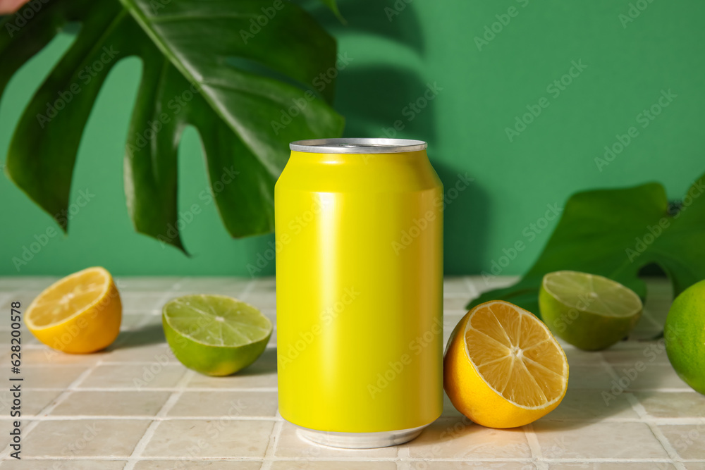 Can of soda with citrus fruits and palm leaf on table near green wall, closeup