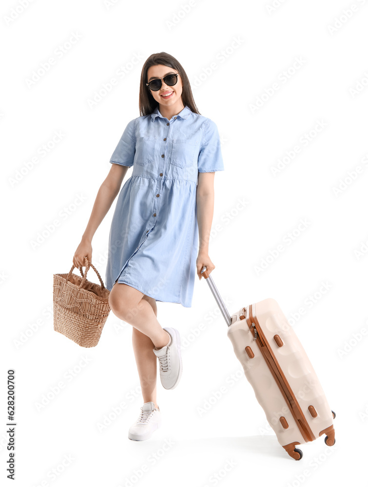 Young woman with beach bag and suitcase on white background