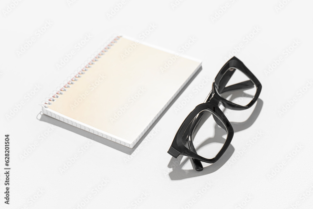 Notebook and black eyeglasses on white background