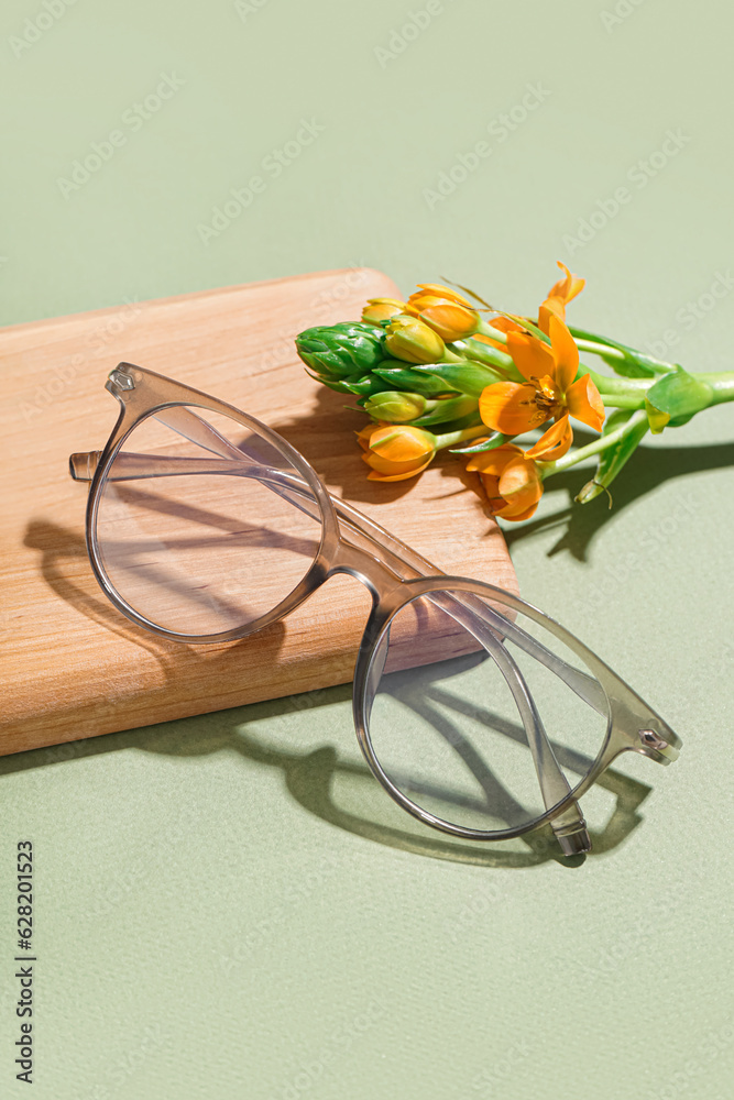 Notebook, flower and eyeglasses on pale green background