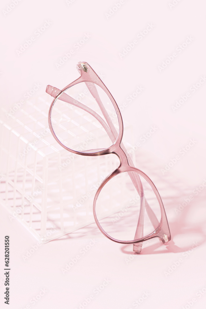 Stylish eyeglasses and plastic box on pale pink background