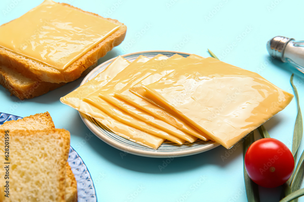 Plates of tasty processed cheese with bread and vegetables on blue background