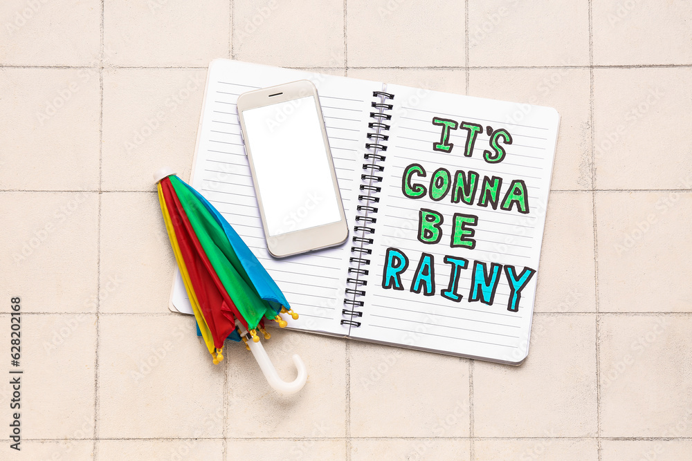 Notebook with text ITS GONNA BE RAINY, mobile phone and umbrella on white tile background. Weather 