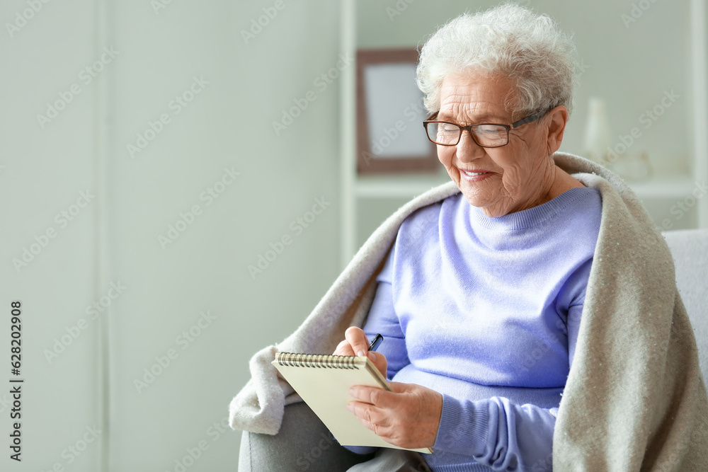 Senior woman writing in notebook at home