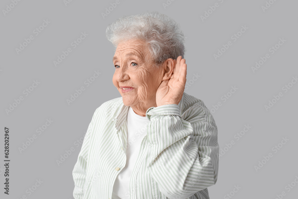 Senior woman trying to hear something on grey background