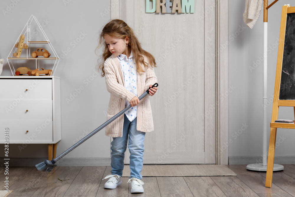 Cute little girl sweeping floor with broom at home