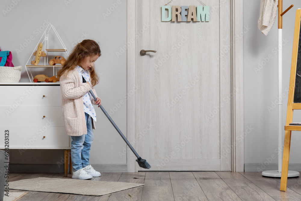 Cute little girl sweeping floor with broom at home