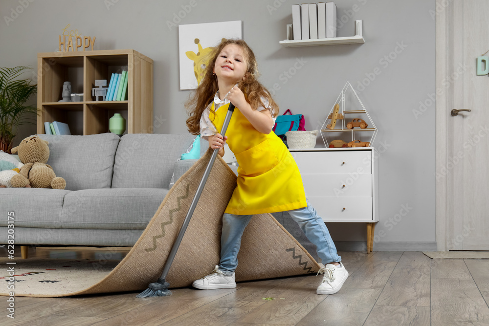 Cute little girl sweeping floor under carpet with broom at home