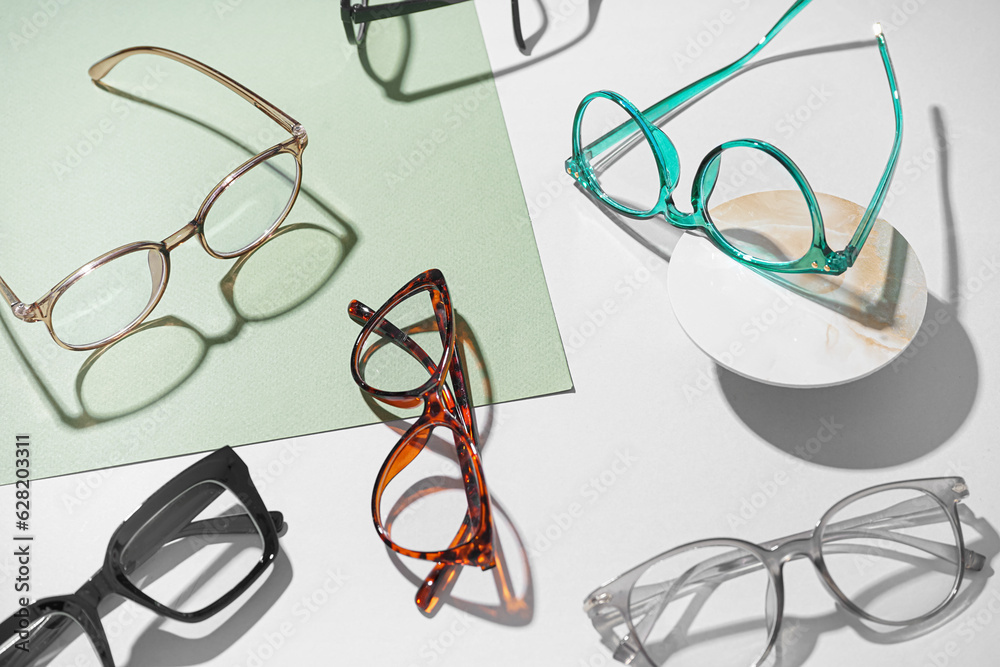 Many different stylish eyeglasses on color background