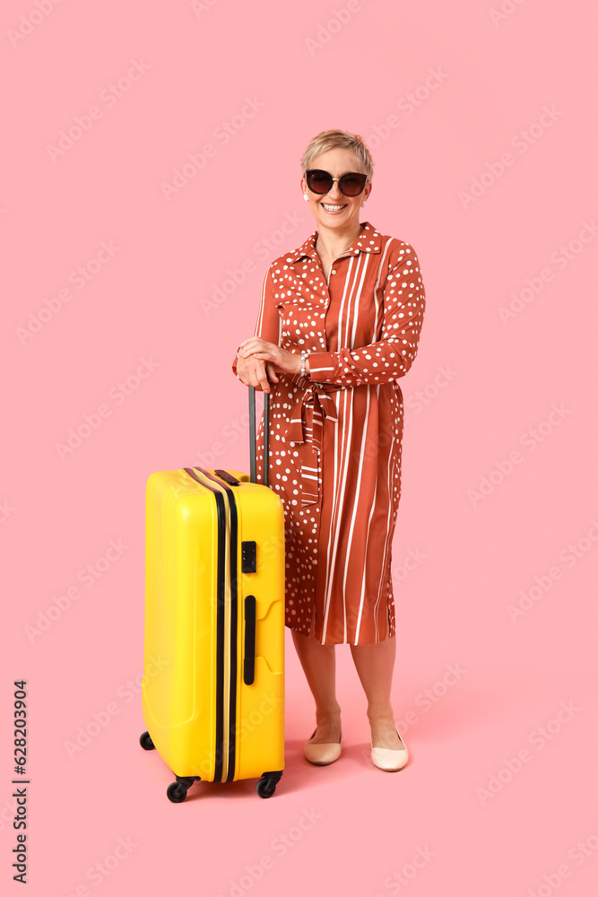 Mature woman with suitcase on pink background