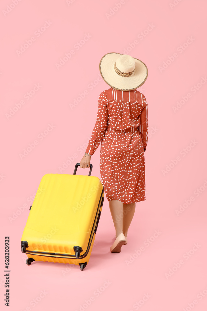 Mature woman with suitcase on pink background, back view