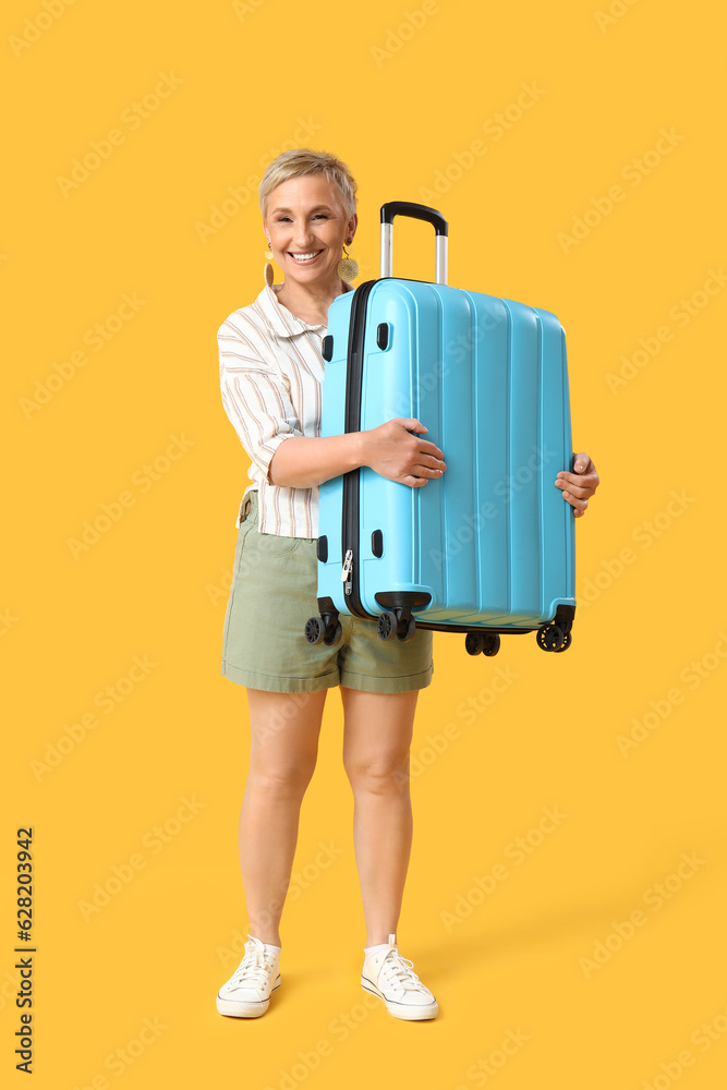 Mature woman with suitcase on yellow background