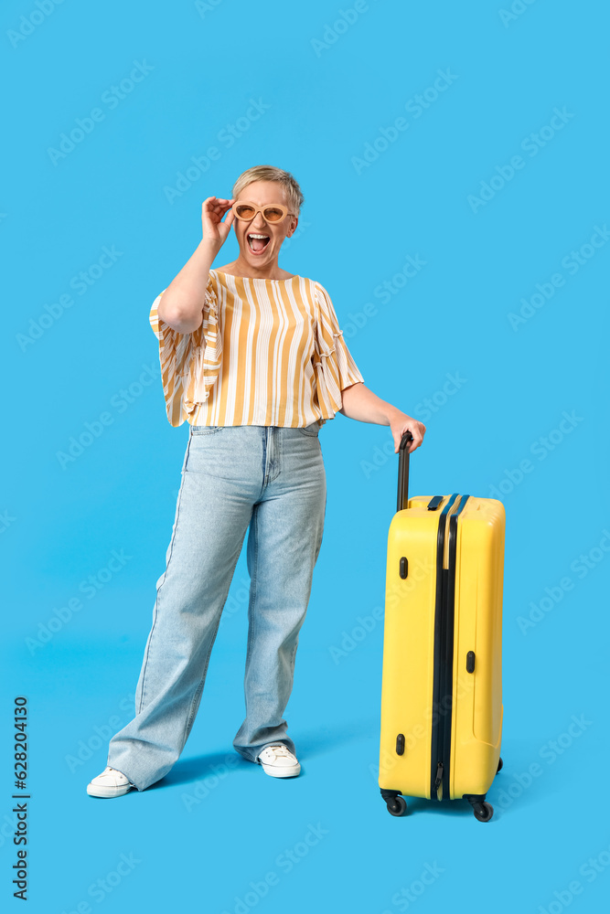 Mature woman with suitcase on blue background