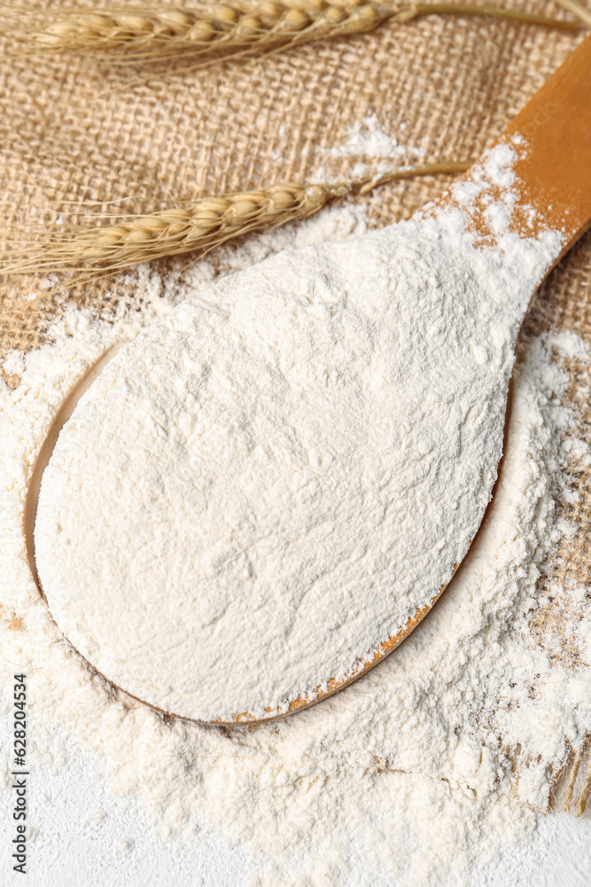 Wooden spoon with flour and wheat ears on white background