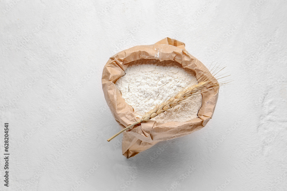 Paper bag with flour and wheat ear on white background