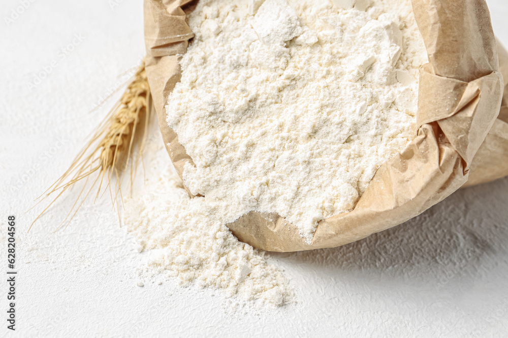 Paper bag with flour and wheat ear on white background