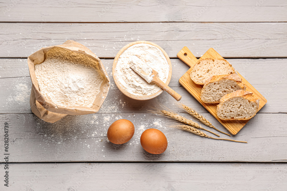 Wooden board with slices of bread, eggs and wheat flour on grey wooden background