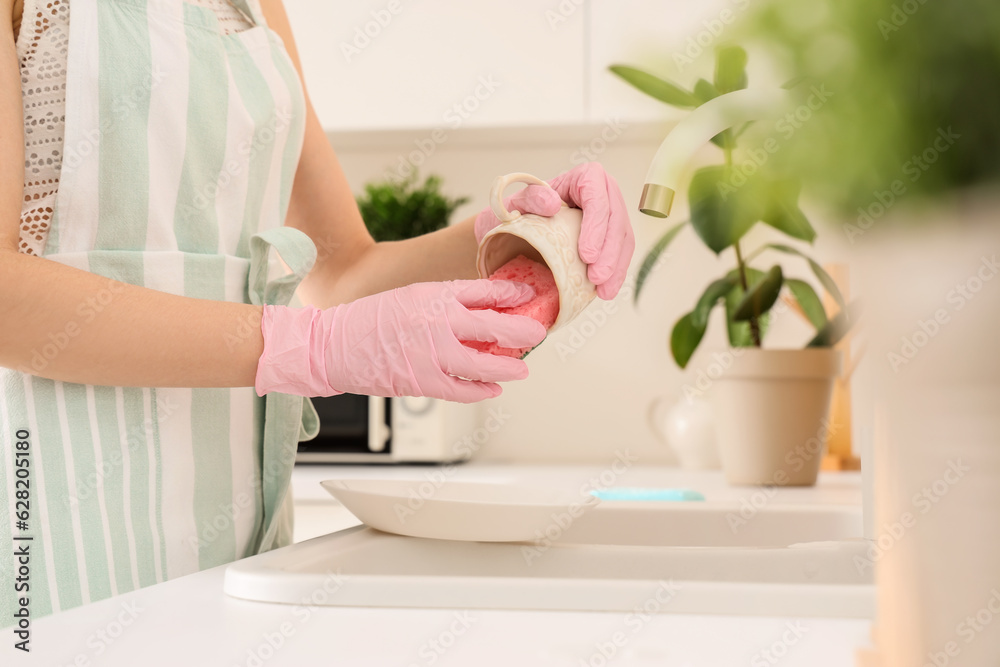 Woman washing cup with sponge in kitchen, closeup