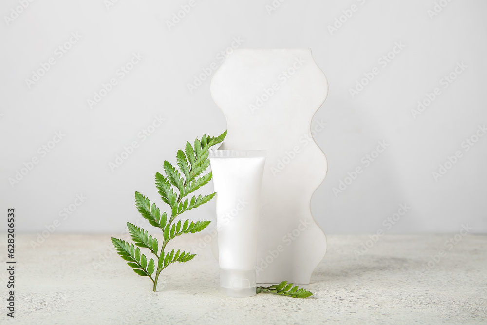 Composition with tube of cosmetic product, plaster podium and fern leaf on light background