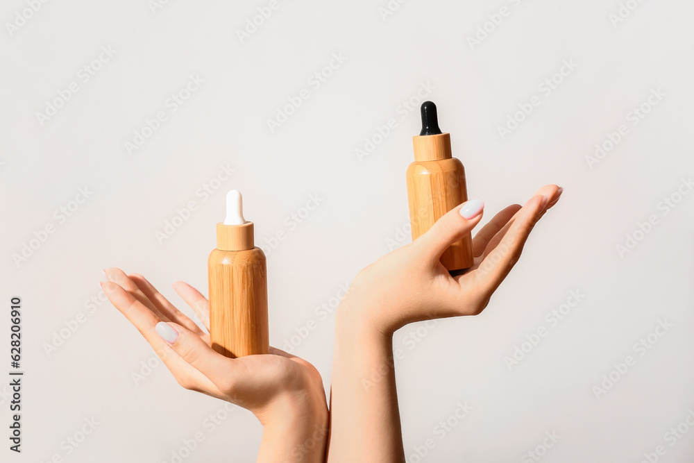 Hands of woman with bottles of cosmetic oil on light background