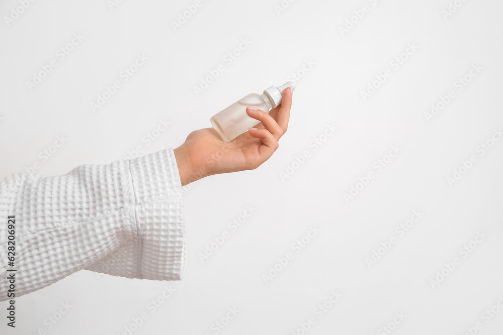 Hand of woman with bottle of cosmetic oil on light background