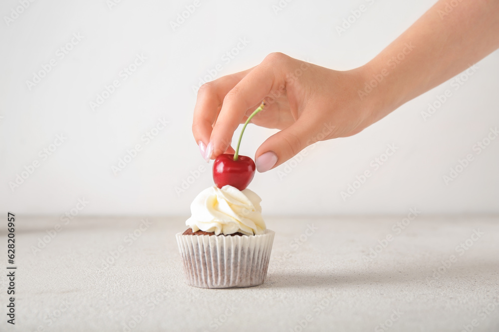 Woman decorating tasty cupcake with cherry on light background