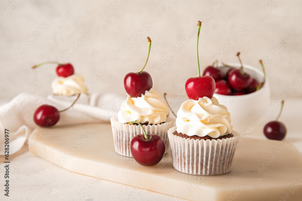 Board with tasty cherry cupcakes on light background