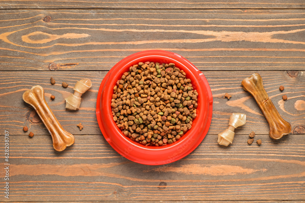 Composition with bowl of dry dog food and treats on wooden background